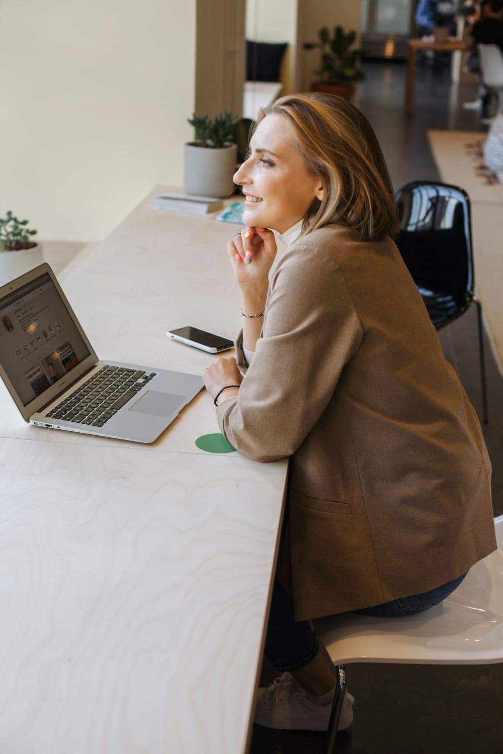 A smiling woman at a long wooden table, a laptop beside her